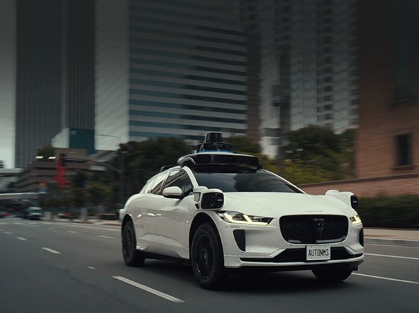 Un robotaxi de Waymo circulando por una avenida entre edificios
