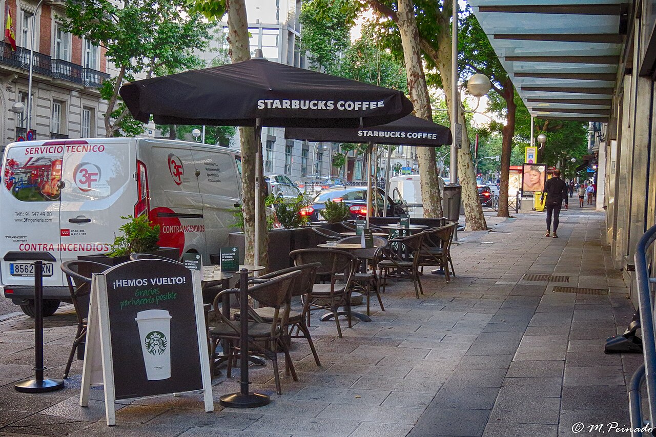 Terraza de una cafetería con mesas, sillas y sombrillas en una calle de Madrid